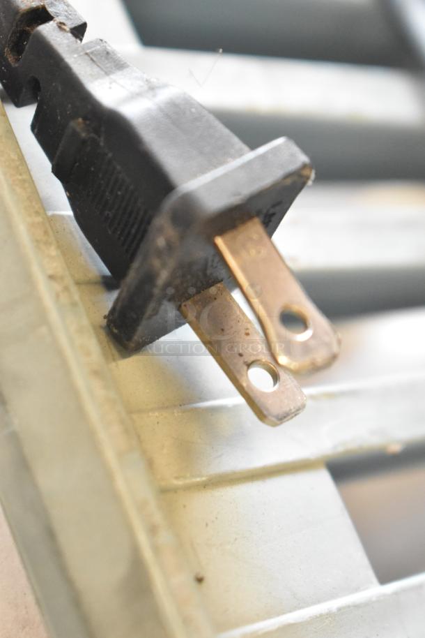 Close-up of a two-prong electrical plug on a metal surface, part of auction items including Zylux PC and Sony speaker.