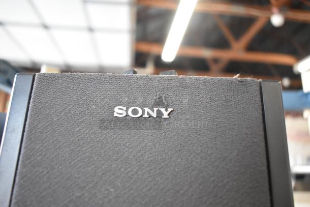 Sony speaker close-up with black fabric grille and silver logo, part of auction lot with six varied items.