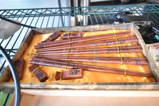 Wooden chopsticks with dragon engravings in a decorative box, resting on an orange silk lining, in good condition.