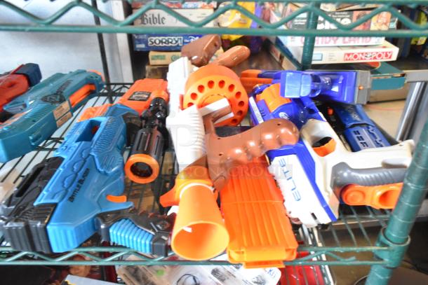 Two-tier lot of various toy guns, including blue, orange models with branding. Items on wire shelf; board games in background.