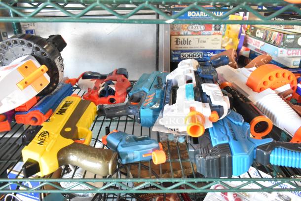 Two-tier wire shelf with assorted toy guns, including Nerf, in mixed condition. Board games and other items visible in the background.