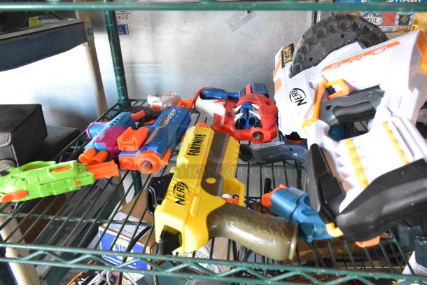 Two-tier shelf with various toy guns, including Nerf models. Toys are in mixed colors and appear in good condition.
