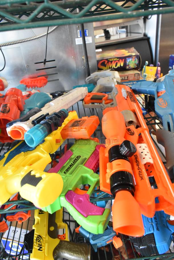 Two-tier shelf with assorted toy guns, including Nerf models, in various colors and conditions. Visible Simon game box.
