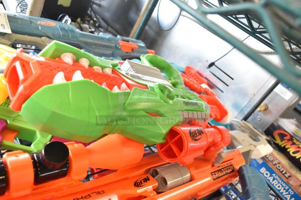 Two tier lot of toy guns, including Nerf models in bright colors, on metal shelf. Variety of styles and designs.