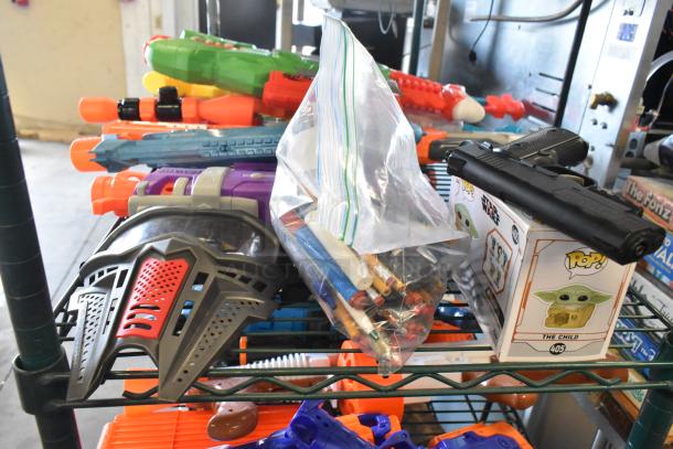 Two-tier lot with various items including colorful toy guns, a black imitation gun, boxed collectible, and craft supplies.