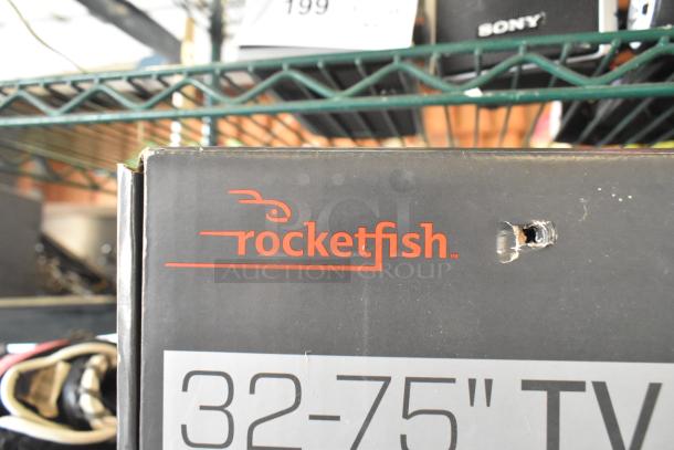 Box of Rocketfish TV mount for 32-75" TVs with visible hole, placed on shelf near various items.
