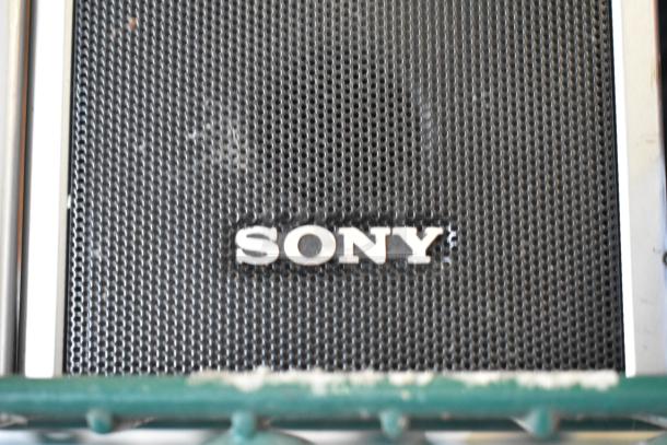Sony speaker with metal grille and logo; part of a two-tier auction lot with additional collectibles and dolls.