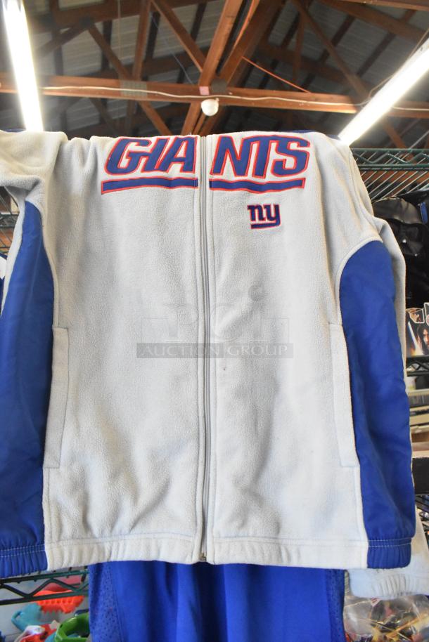 New York Giants zip-up fleece jacket, gray with blue sleeves, features embroidered "GIANTS" and logo, displayed hanging.