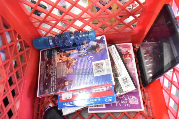 Red basket containing DVDs with colorful covers, a blue toy, and a small electronic device. Items are in mixed condition.