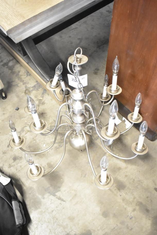 Silver metal chandelier with ten candle-style lights, elegant curved arms, and chain for hanging. Item tag "202".