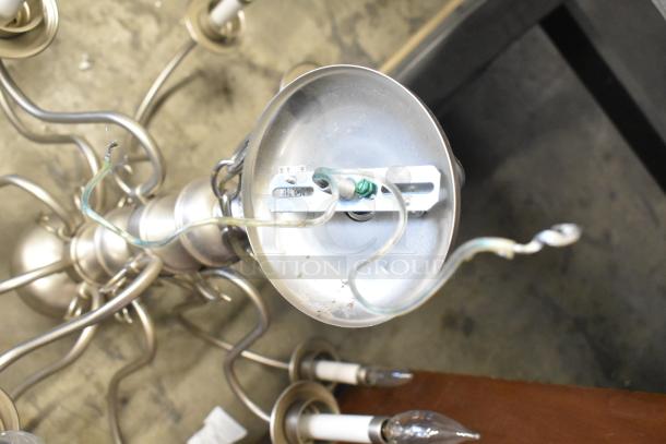 Metal chandelier with curved arms, multiple bulb sockets, and visible wiring. In fair condition.