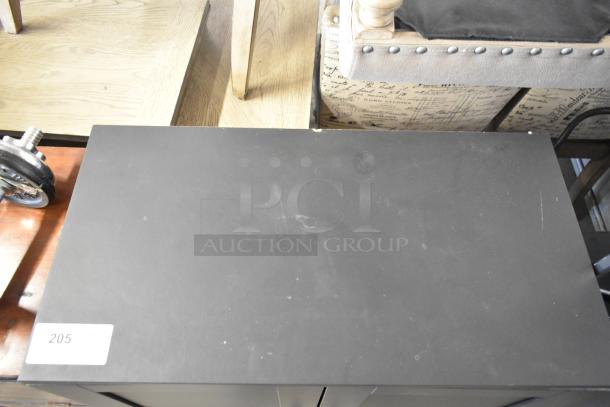 Black 2-door cabinet, top view. Slight surface marks visible. Label with “205” attached. Modern design, likely used condition.