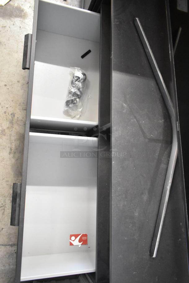 Black television stand with open shelves, one containing a bag of hardware. Good condition, minor dust visible.