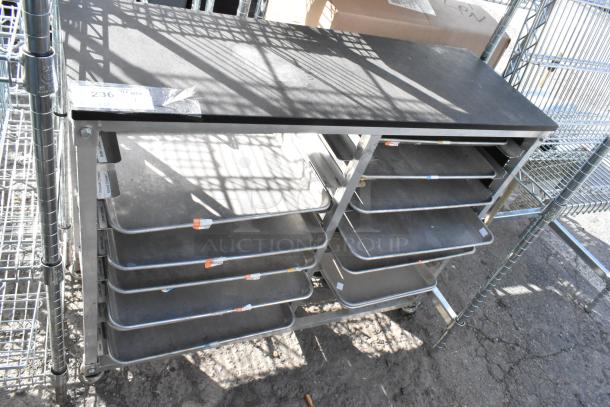 Metal cart with multiple shelves holding metal baking pans, showing visible ID tags. Sturdy construction, used condition.
