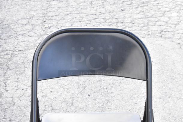 Black folding chair on a concrete surface, part of a set with cart and shelving unit. Good condition. Auction lot of 5 items.