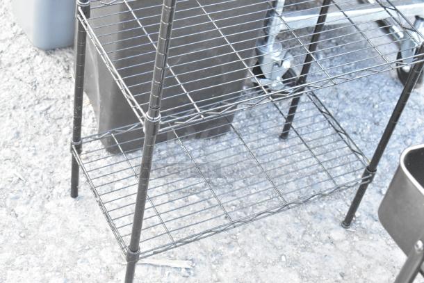 Black wire shelving unit with three shelves, part of a lot of five items including a folding chair and cart. Items are in fair condition.