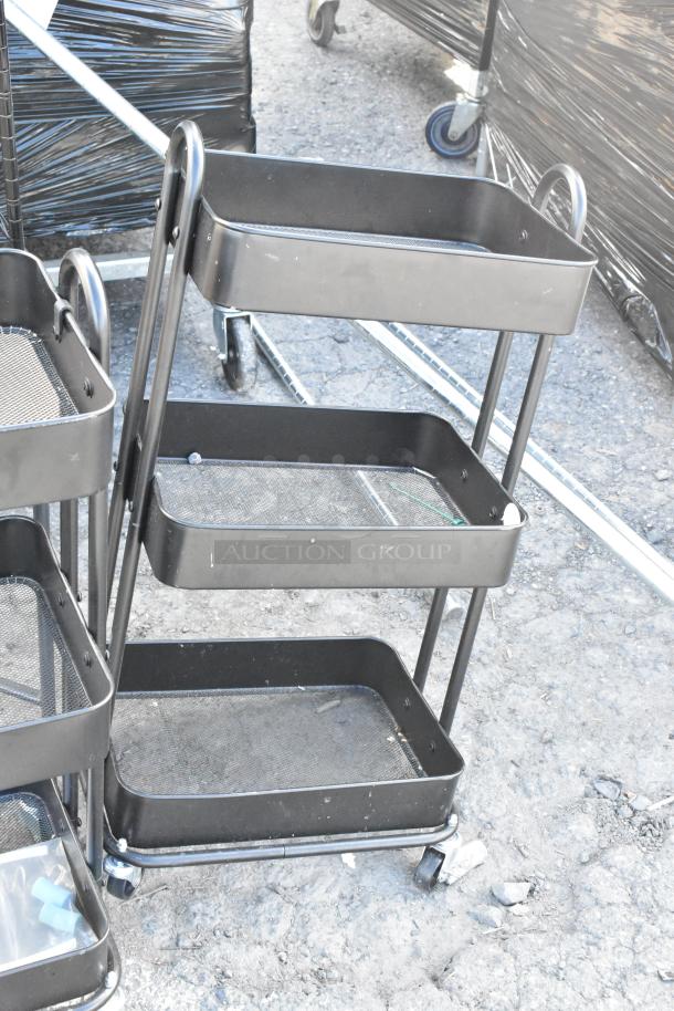 Black metal cart with three mesh shelves, on wheels. Part of a 5-item auction lot, including a folding chair and shelving unit.