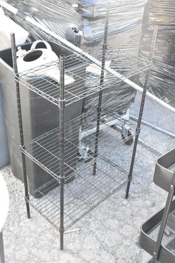 Black wire shelving unit with three tiers, shown outdoors. Includes sturdy metal frame. Good condition.