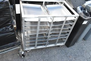 Commercial metal pan transport rack with multiple metal baking pans and casters, showing signs of use.