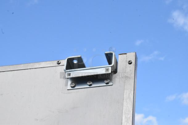 Metal swinging kitchen door with a sturdy silver hinge, showing moderate wear and secure fastening, against a blue sky.