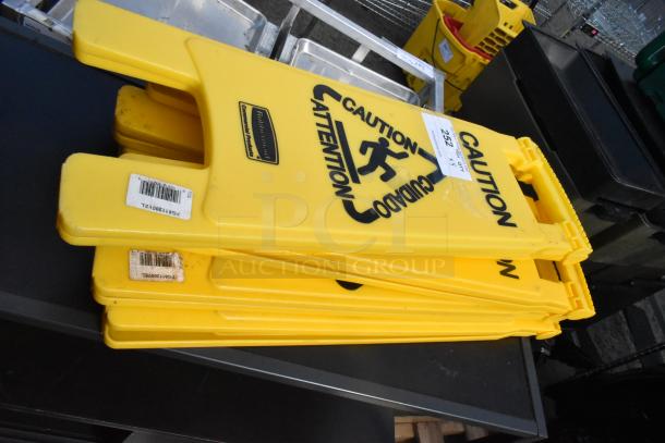 Five yellow Rubbermaid wet floor caution signs, stacked. Features safety icon and bilingual text. Good condition.