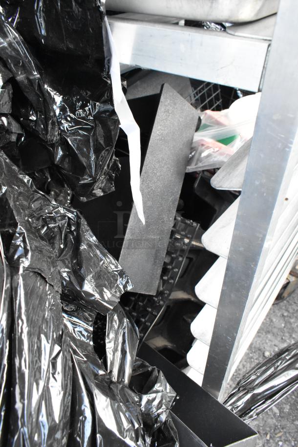 Metal commercial pan transport rack on casters, filled with various kitchen items, partially obscured by black plastic.