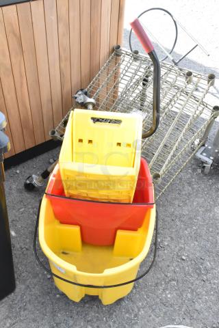 Yellow poly mop bucket with a red wringing attachment, commercial casters for mobility, some signs of use.