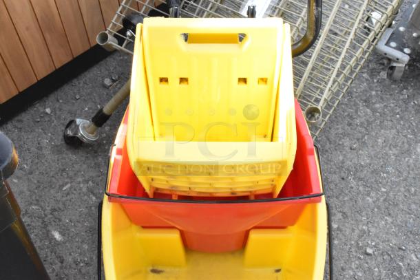 Yellow poly mop bucket with wringing attachment, mounted on commercial casters, showing visible wear and use.