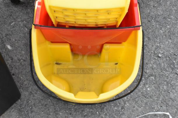 Yellow poly mop bucket with wringing attachment, commercial casters; shows signs of use, ideal for cleaning tasks.