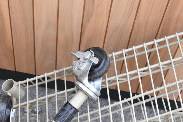 Tan wire shelving unit on commercial casters, featuring four tiers and sturdy poles, displayed against a wooden backdrop.