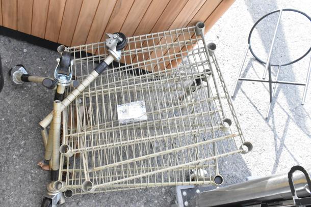 Tan 4-tier wire shelving unit with poles, commercial casters shown detached, item tag reading "266". Used condition.
