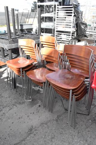 25 wooden dining height chairs with chrome finish frame, stacked outdoors. Shows signs of use.