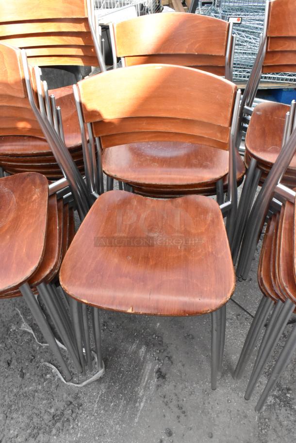 25 wooden dining-height chairs with chrome finish frame, stacked in used condition; signs of wear visible.