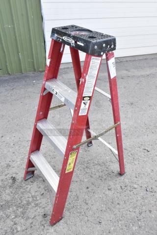 Werner A Frame Ladder, red, three-step, fiberglass construction, visible safety labels, minor paint marks, rugged condition.