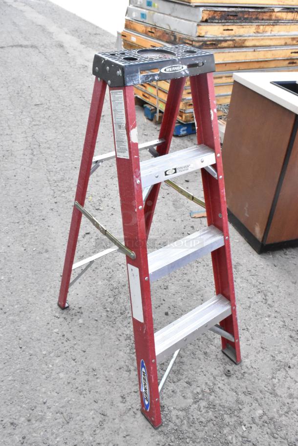 Werner A Frame Ladder, red frame, black top, metal steps, visible labels, used condition, sturdy design.