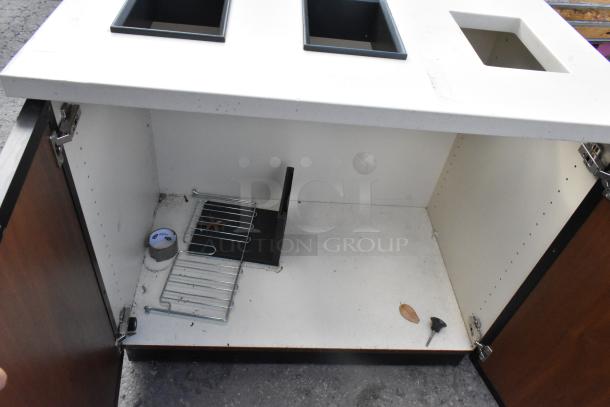 Wood pattern trash can shell with three trash deposit holes, open cabinet doors, and a shelf. Minimal signs of wear.