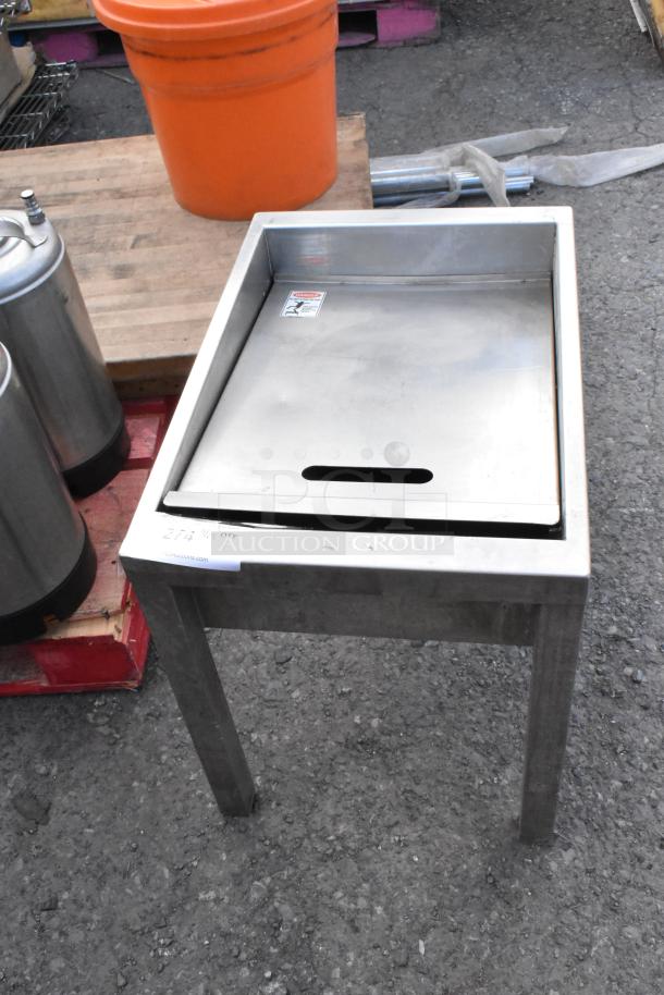 Metal bin on legs with a flat lid, stainless steel finish, visible warning label, and slight surface wear.