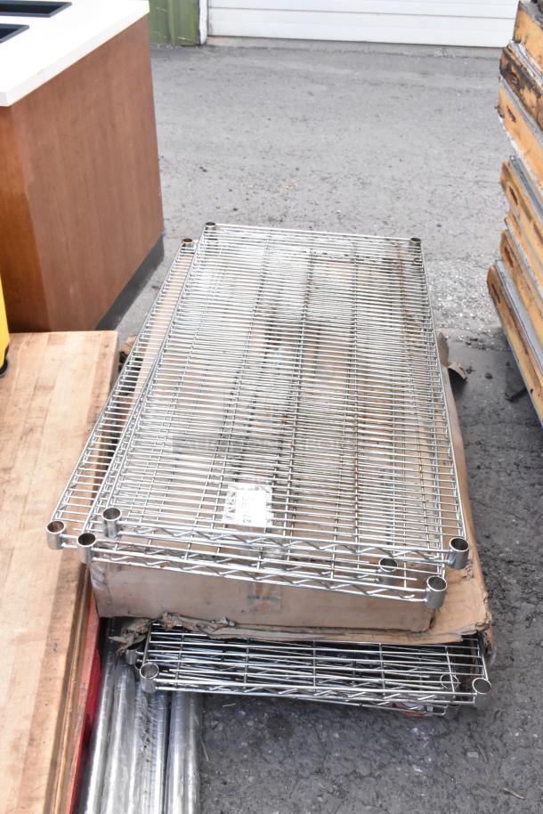Lot of chrome finish wire shelves, stacked and labeled, show signs of wear, ideal for storage solutions.