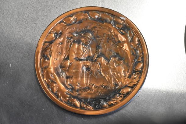 Bronze decorative plate with embossed soldier and dog scene, showing light wear. Suitable for display or collection.
