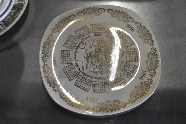 Vintage ceramic plate with a 1956 calendar design and gold floral border, featuring a central illustration, excellent condition.