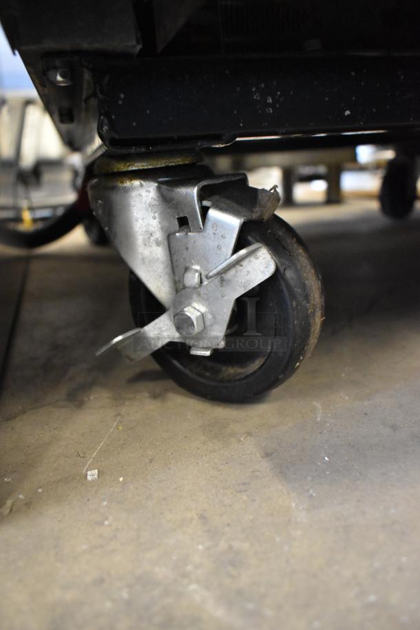 Close-up of a caster wheel on a 2022 True T-23F-HC stainless steel commercial freezer, showing locking mechanism and metal construction.