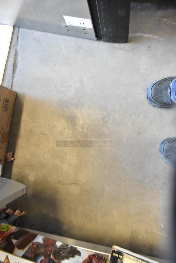 Industrial floor with the edge of a stainless steel commercial appliance, possibly a True freezer model T-23F-HC.