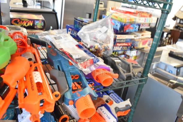 Two-tier shelf with various items including toy guns, board games, and packaged accessories, auctioned as a single lot.