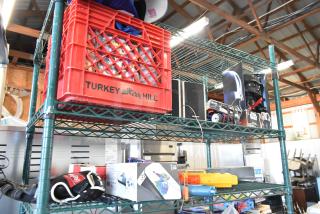 Two-tier shelf with various items including Sony speakers, Star Wars Darth Vader doll, toy truck, and sports jerseys.