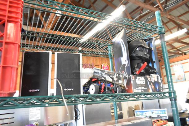Two-tier auction lot with Sony speakers, Jacob doll, Star Wars Darth Vader doll, and jerseys on metal shelves.