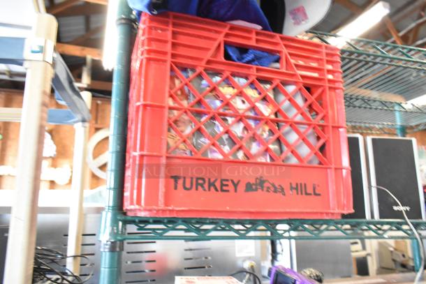 Red Turkey Hill crate with assorted items including a Sony speaker and visible dolls. Crate on a metal shelf.
