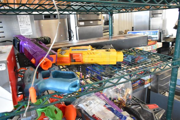 Two-tier shelf with assorted items: colorful toy guns, board games, and packaged items. Includes Sony speaker, dolls.