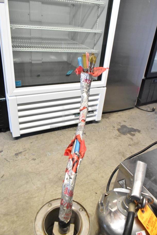 Metal commercial 4 tap beer tower with hoses wrapped in protective foil and red tape, shown near refrigeration units.