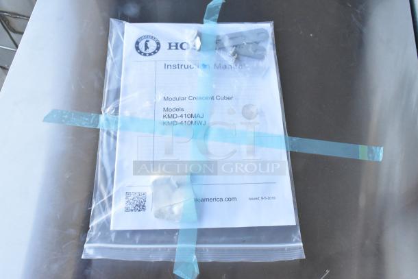 Hoshizaki instruction manual for KMD-410MAJ model in plastic wrap on stainless steel surface.