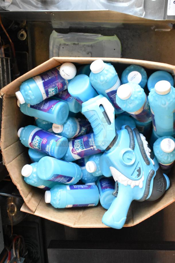 Assorted lot featuring Fom Concentrate bottles and a blue bubble gun, both in new condition, displayed in a cardboard box.